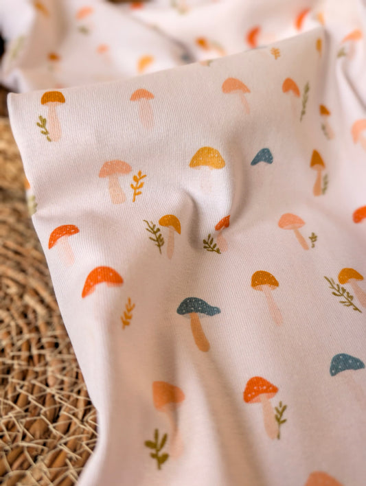 Cotton rib fabric draped on rattan showing scattered toadstool and botanical print — Wren in terracotta, mustard, teal and peach on white